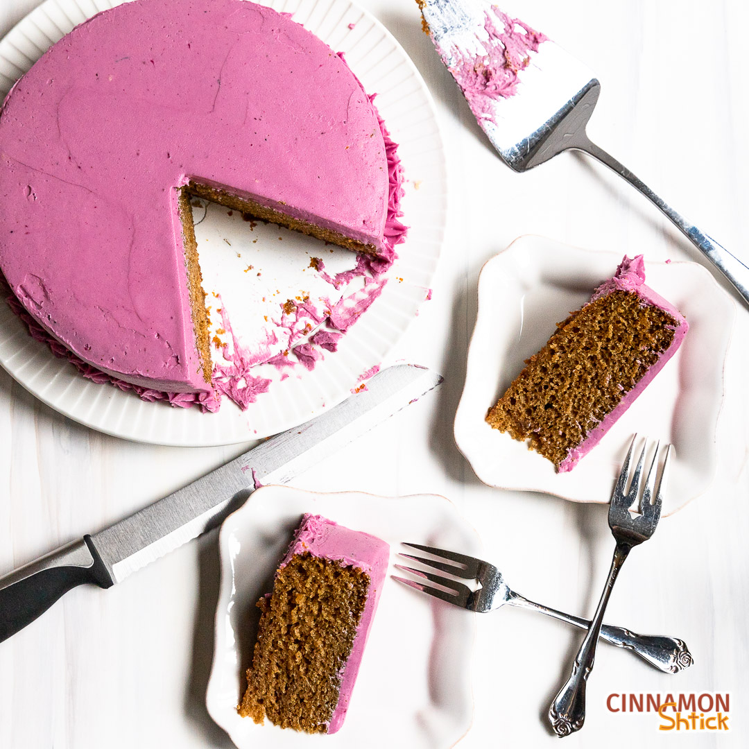 Two plated slices of spice cake with blueberry frosting with rest of cake. 