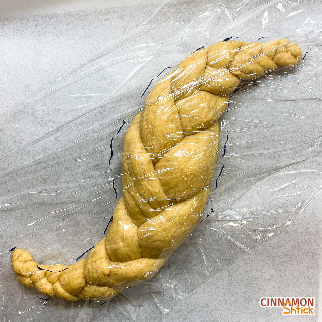 shaped sourdough challah with plastic wrap on it and markings to show its size