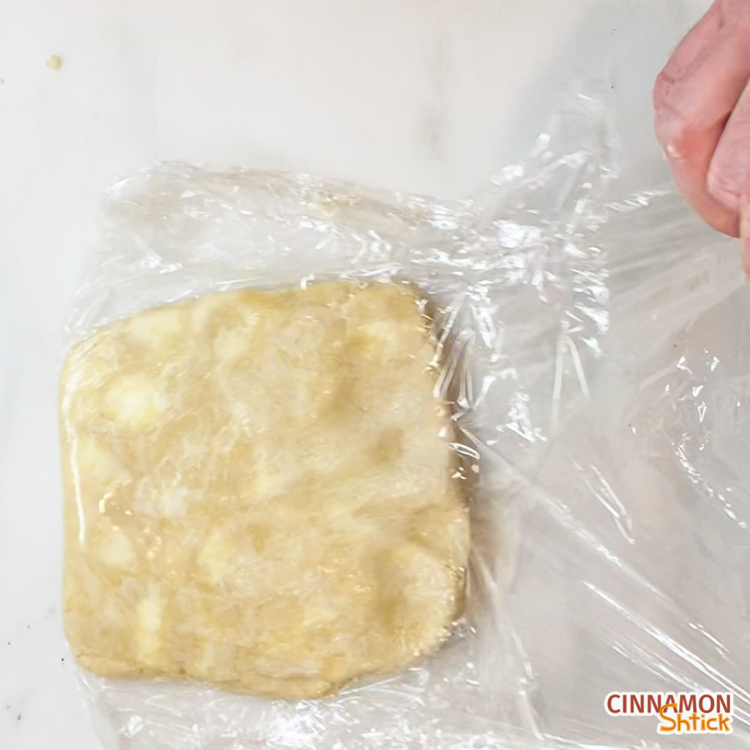 block of dough with noticeable pieces of butter in it being unwrapped from plastic wrap after taken out of refrigerator