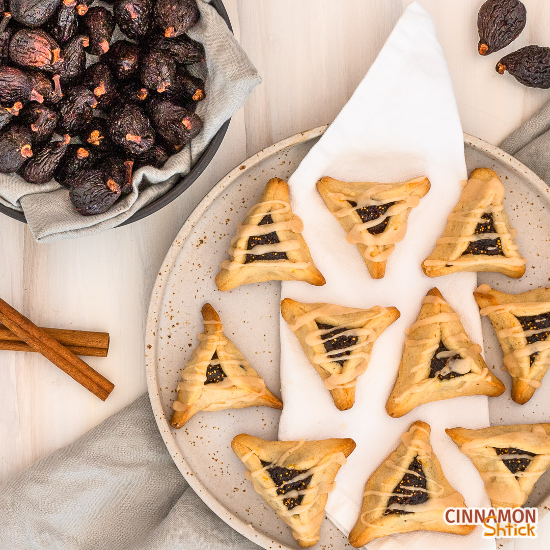 plate of fig hamantaschen with bowl of figs and two cinnamon sticks