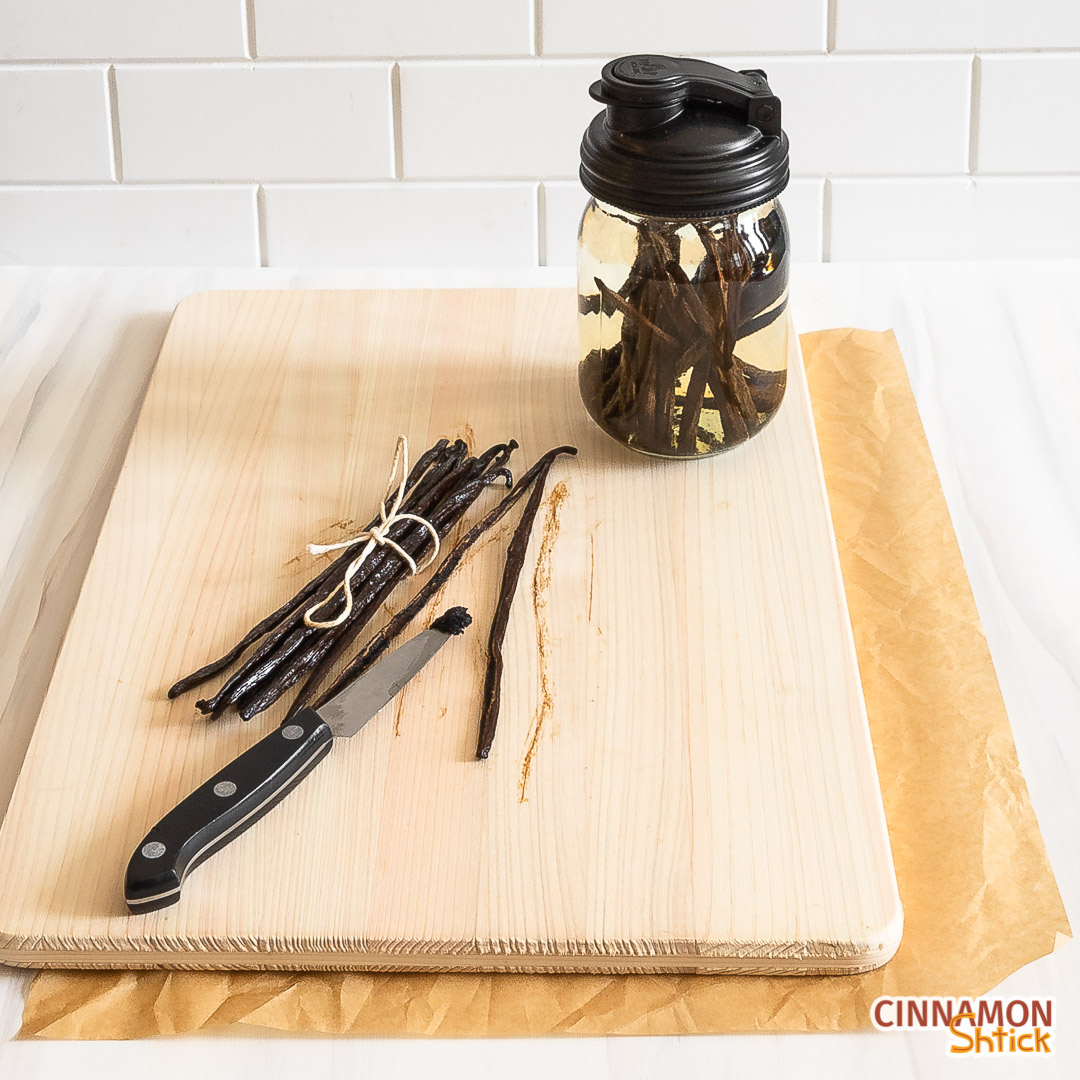 Vanilla beans on a cutting board with a mason jar with a reCAP lid holding alcohol and vanilla beans