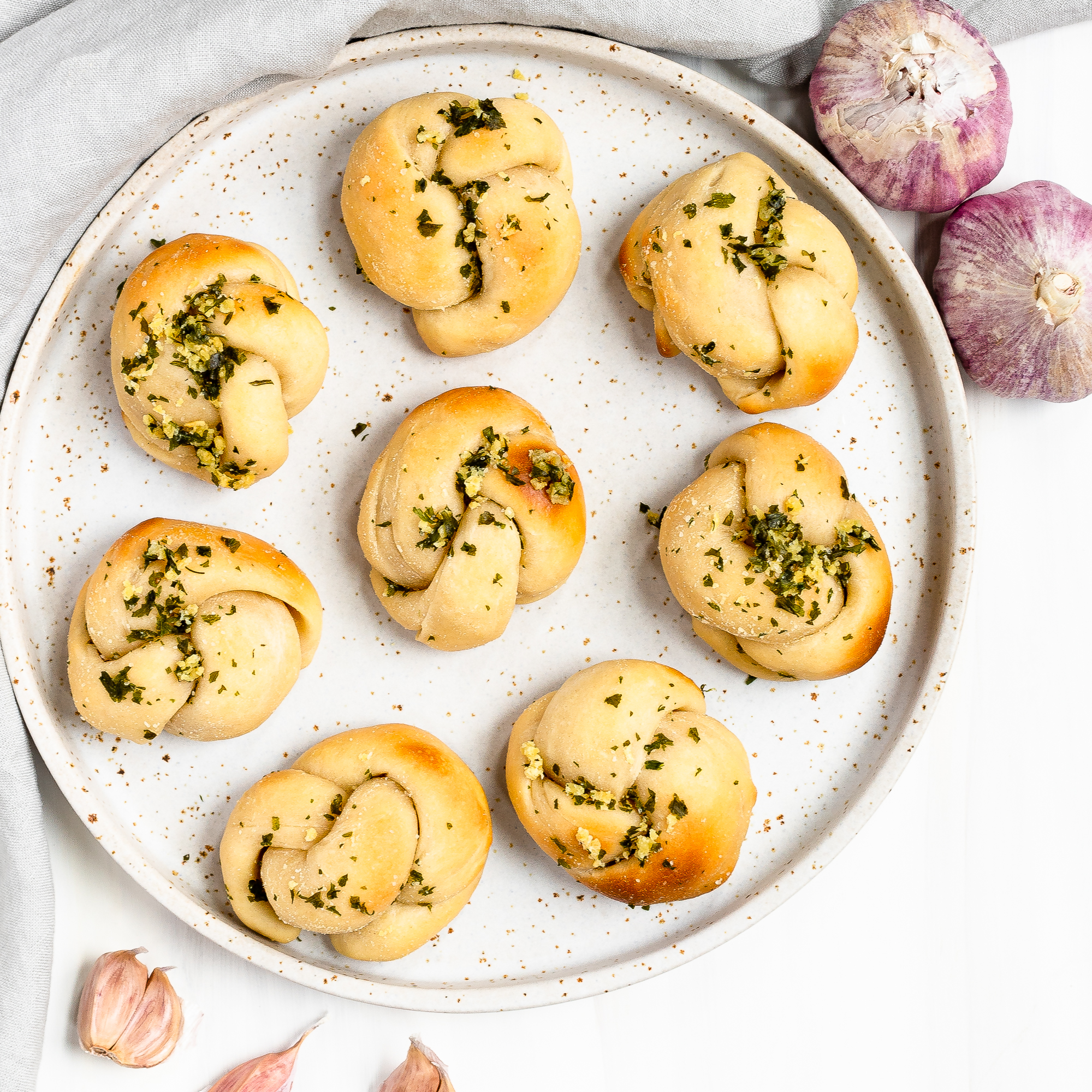8 sourdough discard garlic knots on a plate with some purple garlic surrounding the plate