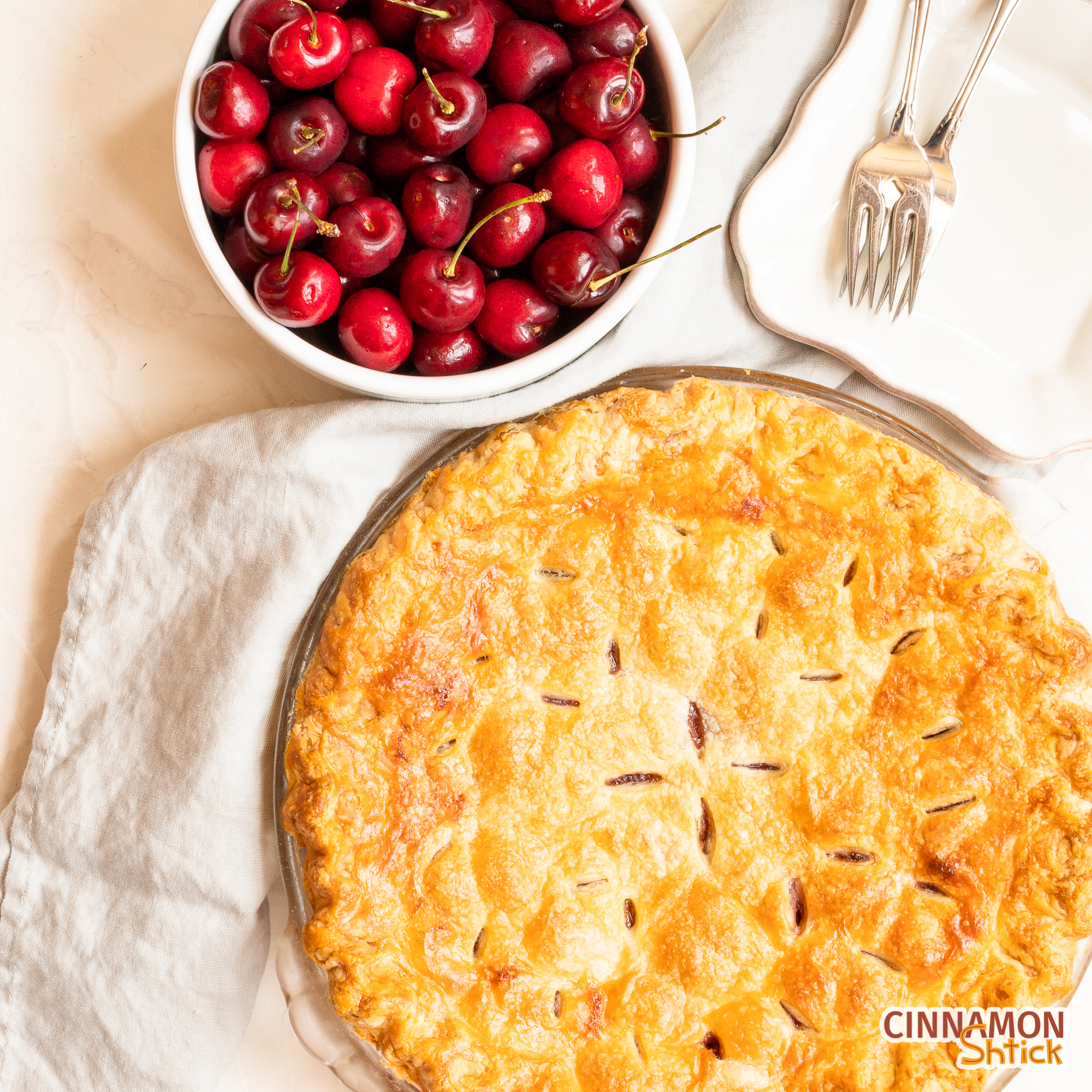 overhead view of cherry pie with bowl of cherries in upper portion