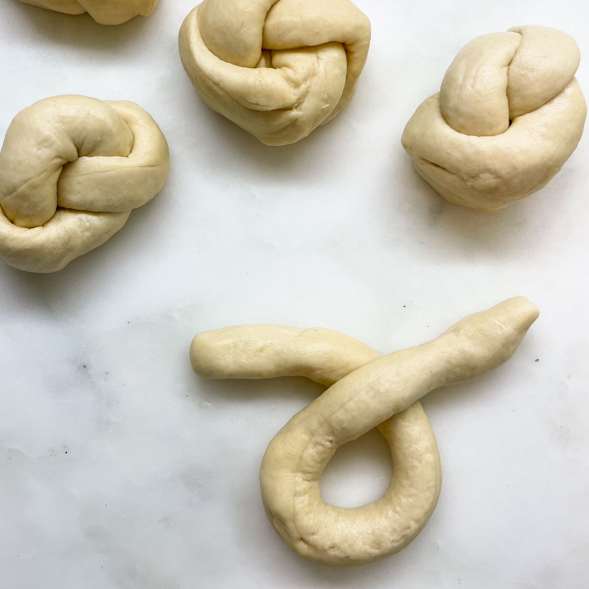 three sourdough discard garlic knots in background with a rope of dough looped over itself showing how to make the knot