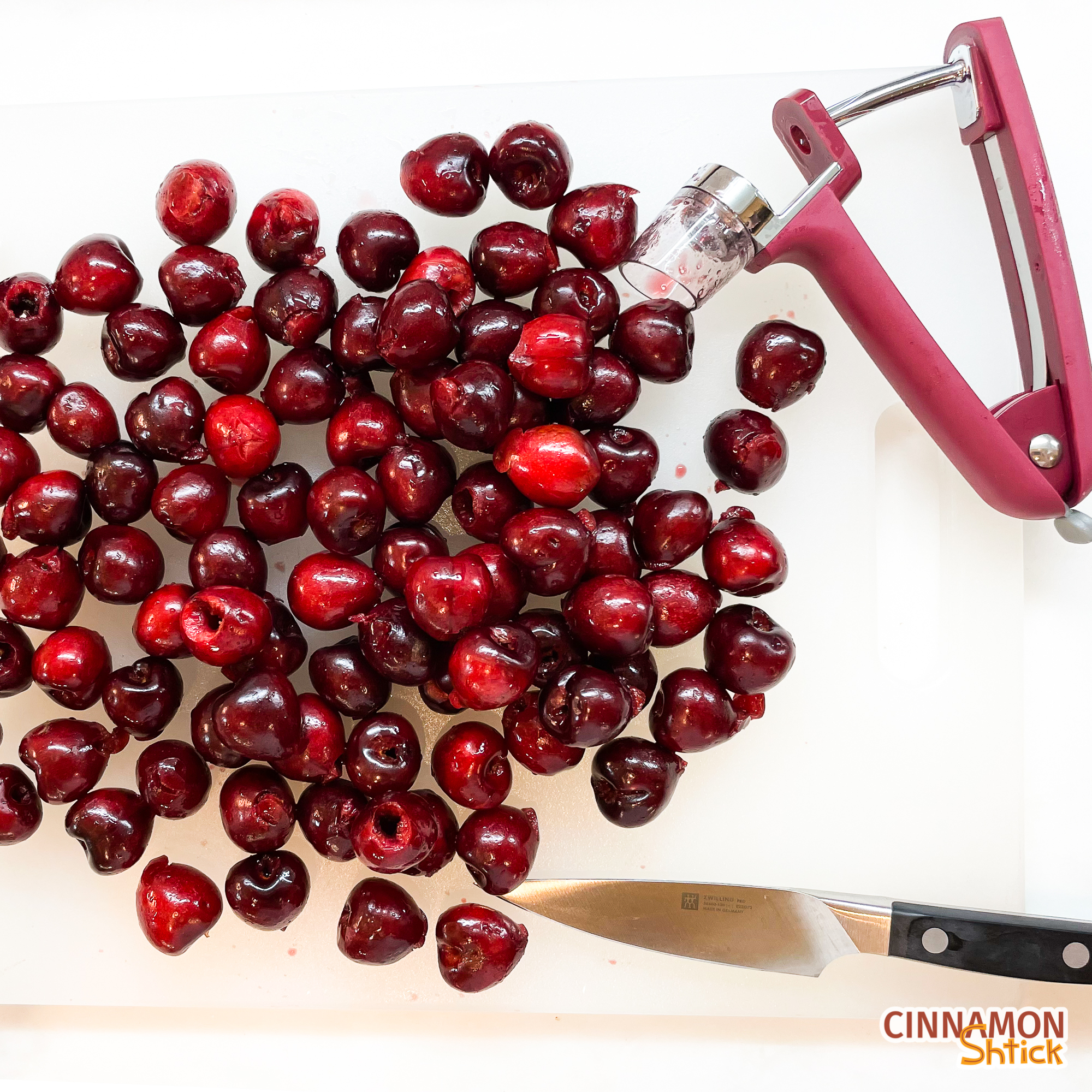 Pitted cherries on cutting board with cherry pitter and a paring knife