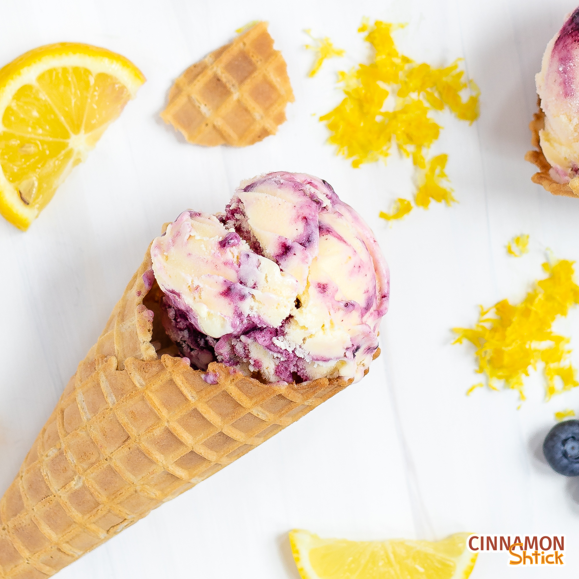 overhead view of a waffle cone filled with lemon blueberry ice cream, lemon wedges, zest and a blueberry