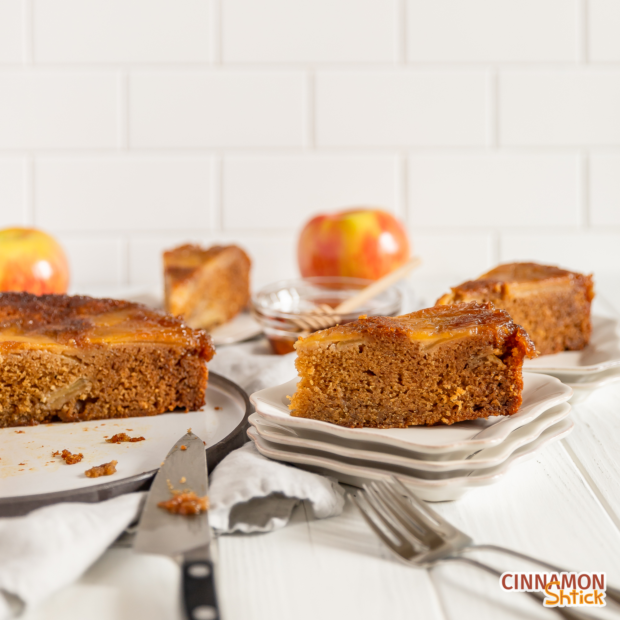 slice of honey upside down apple cake with two other slices in background and rest of cake with an apple