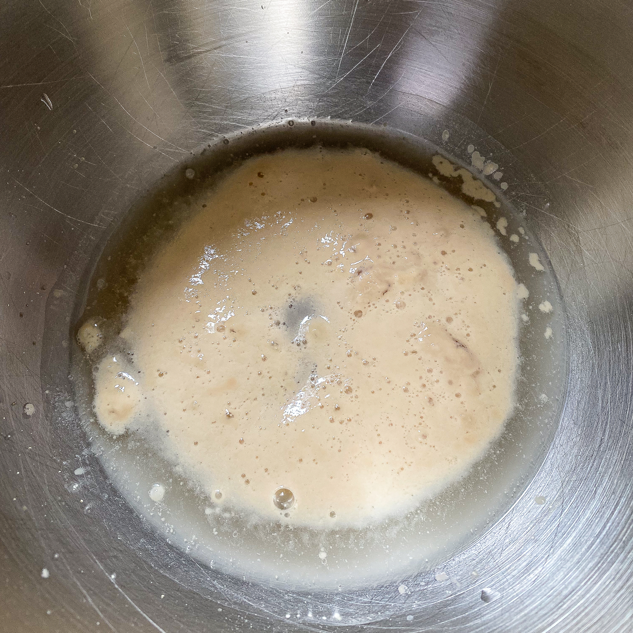 Overhead view of active dry yeast mixed with water bubbling in mixing bowl.