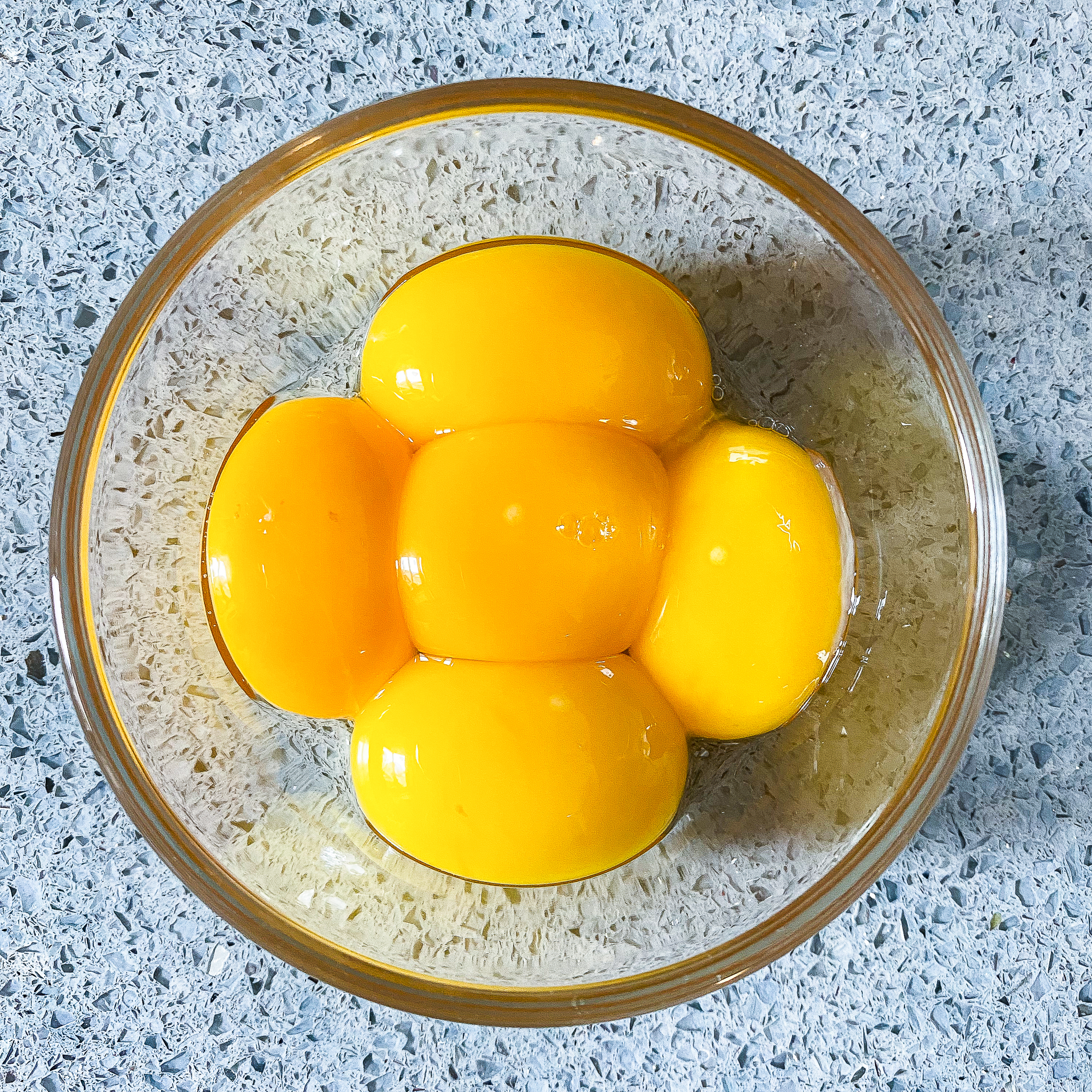 Overhead view of 5 egg yolks in a glass bowl