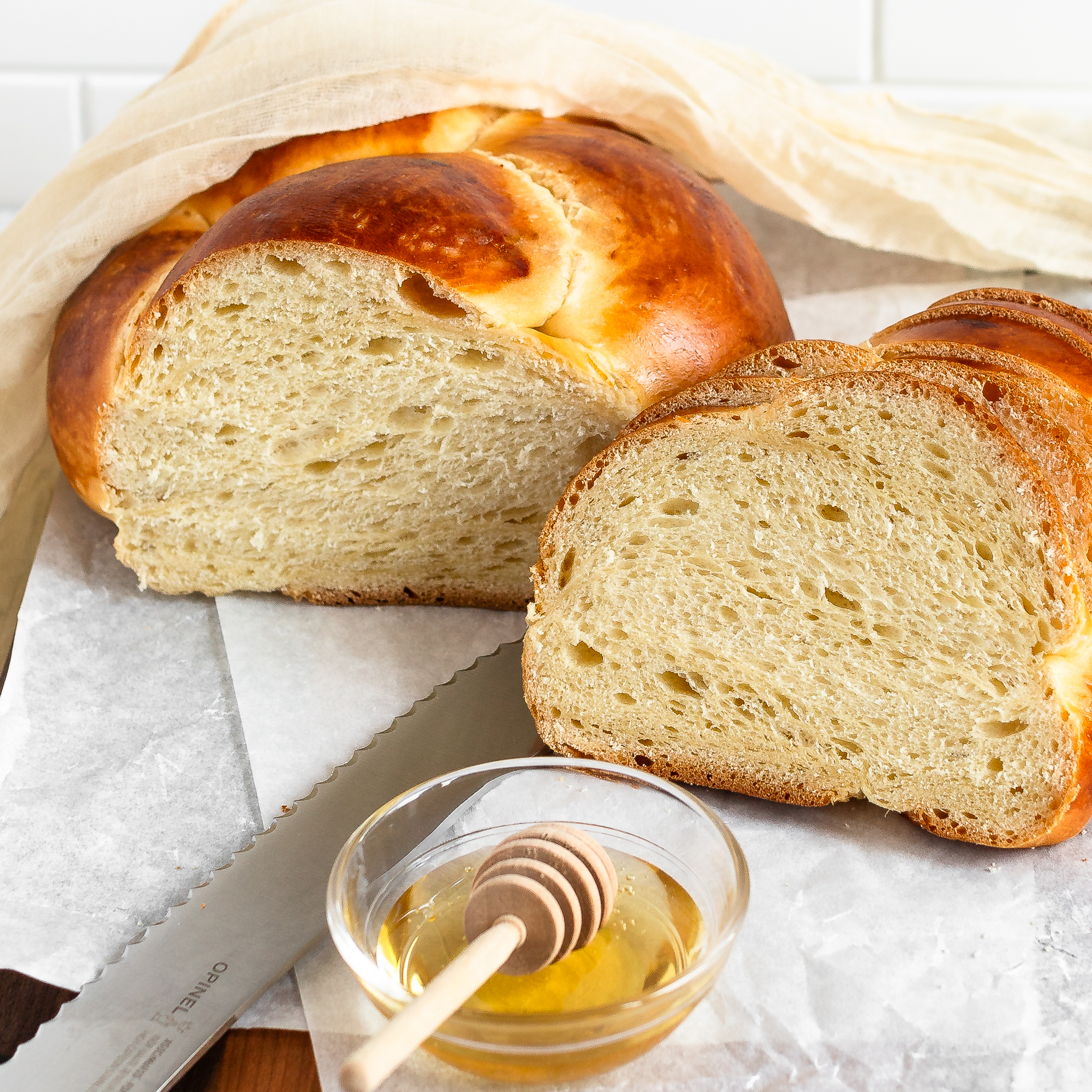 challah sliced on cutting board showing the inside with a bread knife and small bowl of honey in the foreground