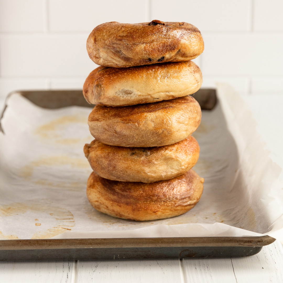 stack of 5 cinnamon raisin bagels on a baking sheet lined with parchment paper