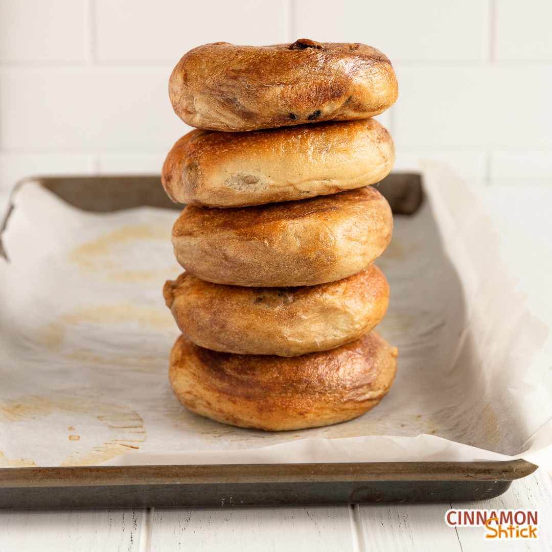 stack of 5 cinnamon raisin bagels on a parchment lined baking sheet