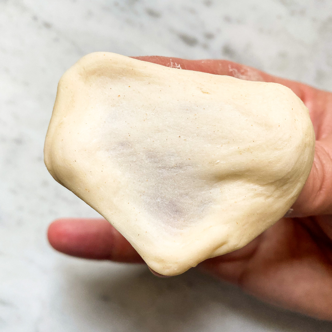 piece of bagel dough stretched out showing the windowpane test