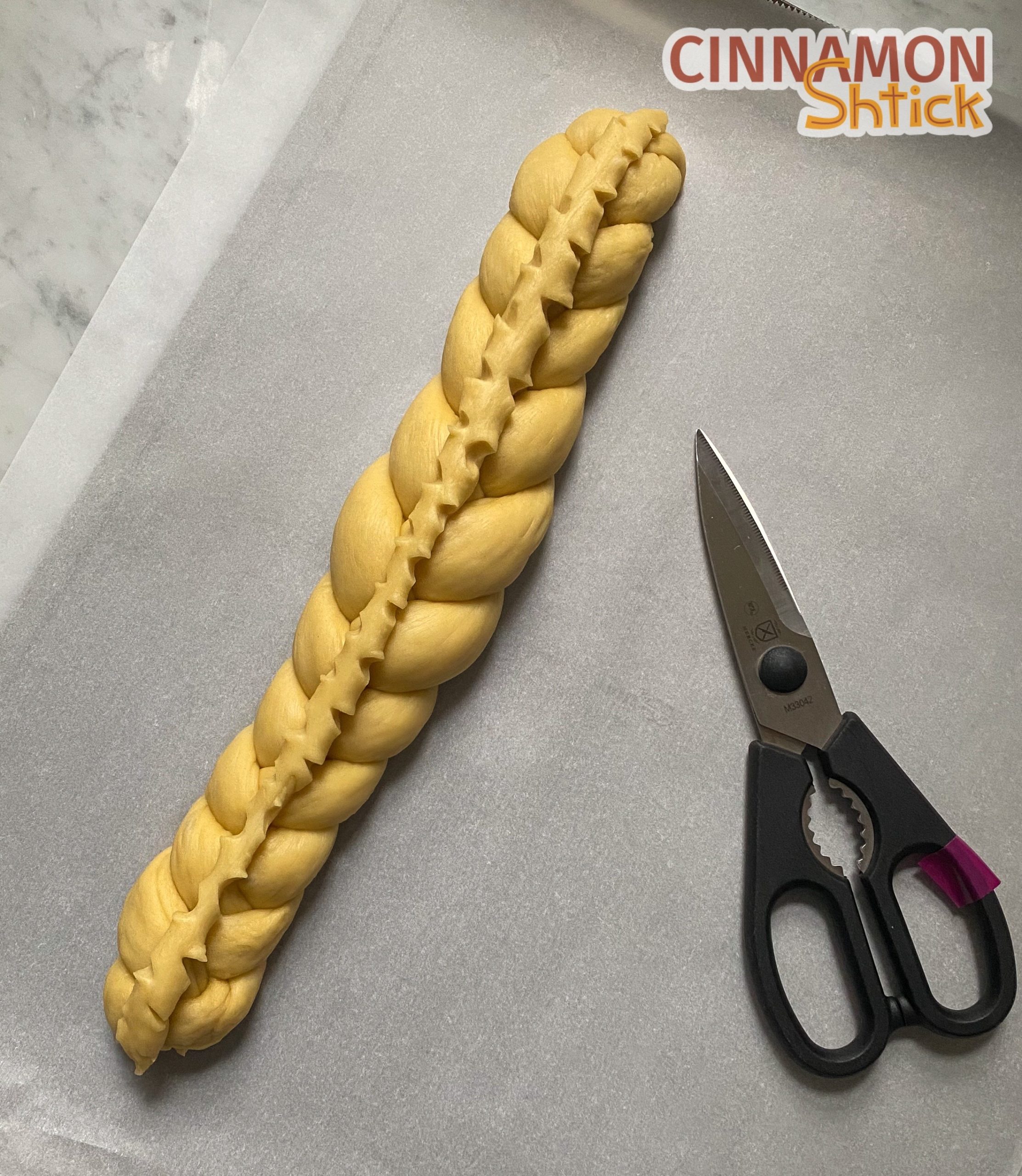 Three strand braided challah with a top line of dough decoratively cut with scissors. 