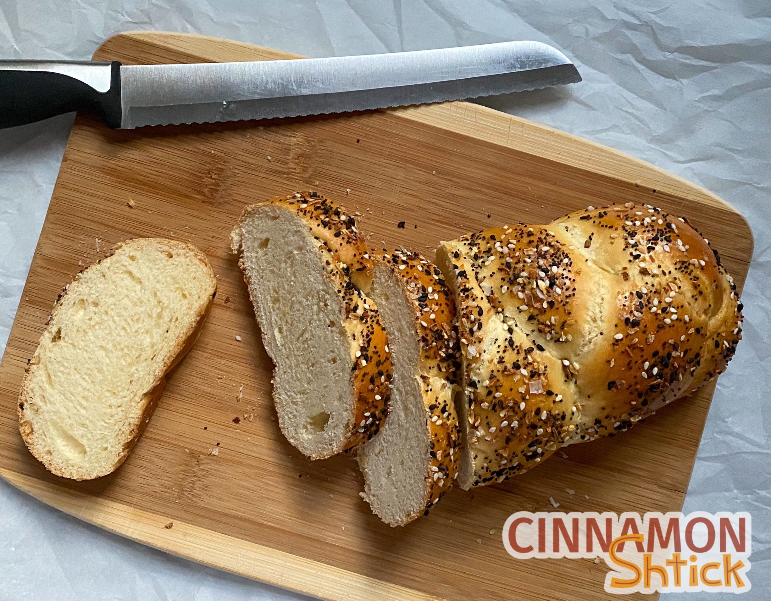 Challah and three slices on cutting board with knife. Challah is covered in everything spice.