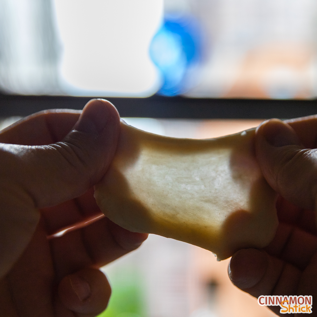 small piece of dough being stretched apart showing that it is translucent without ripping and therefore passing the windowpane test