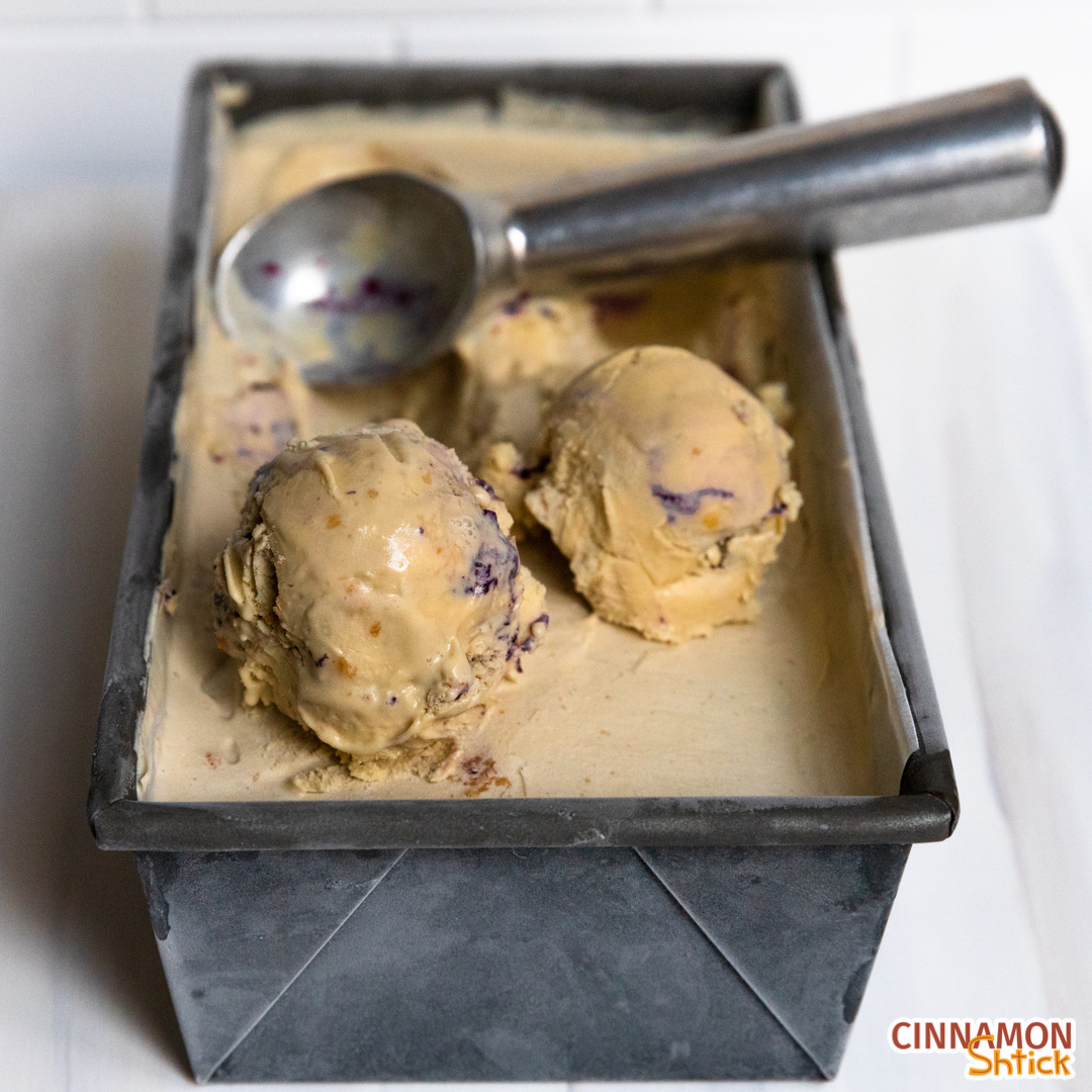 Container of Maple Blueberry Pie Ice Cream with two scoops in front and the ice cream scoop sitting in container behind the scoops.