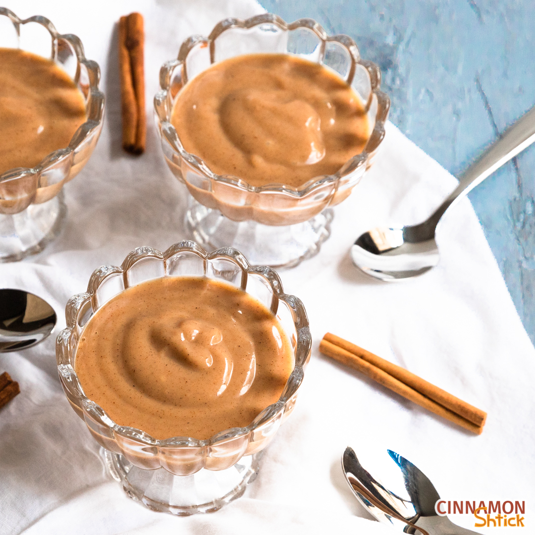 Several dishes of vegan cinnamon pudding on table with spoons and cinnamon sticks.