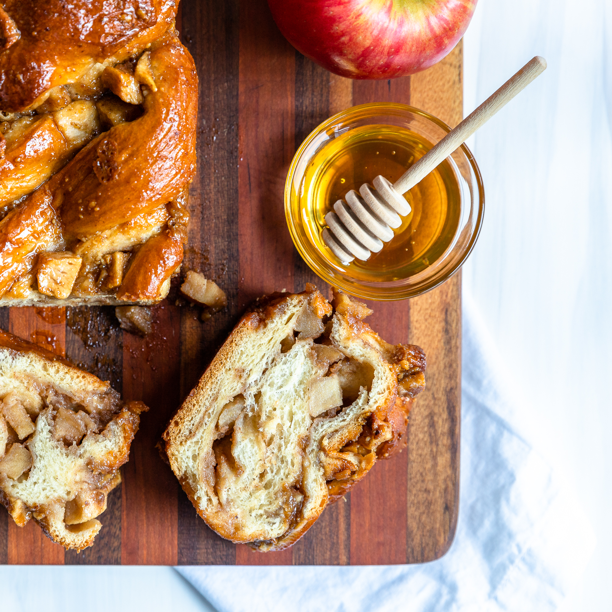 Overhead view of apple honey babka on a cutting board with a. couple of slices laying flat and a bowl of honey and an apple