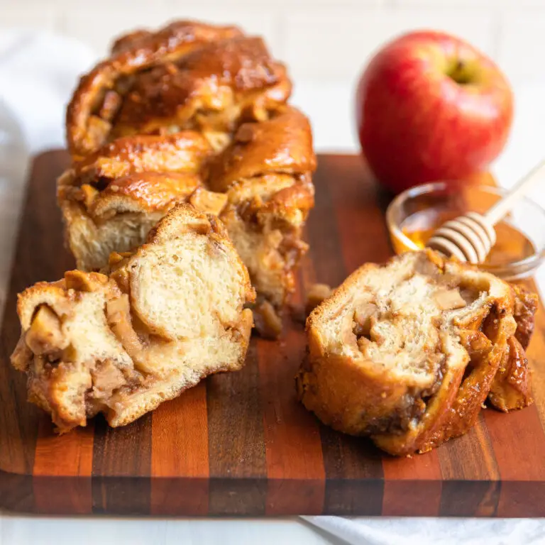 apple honey babka on cutting board with a couple slices showing the inside, a bowl of honey and an apple