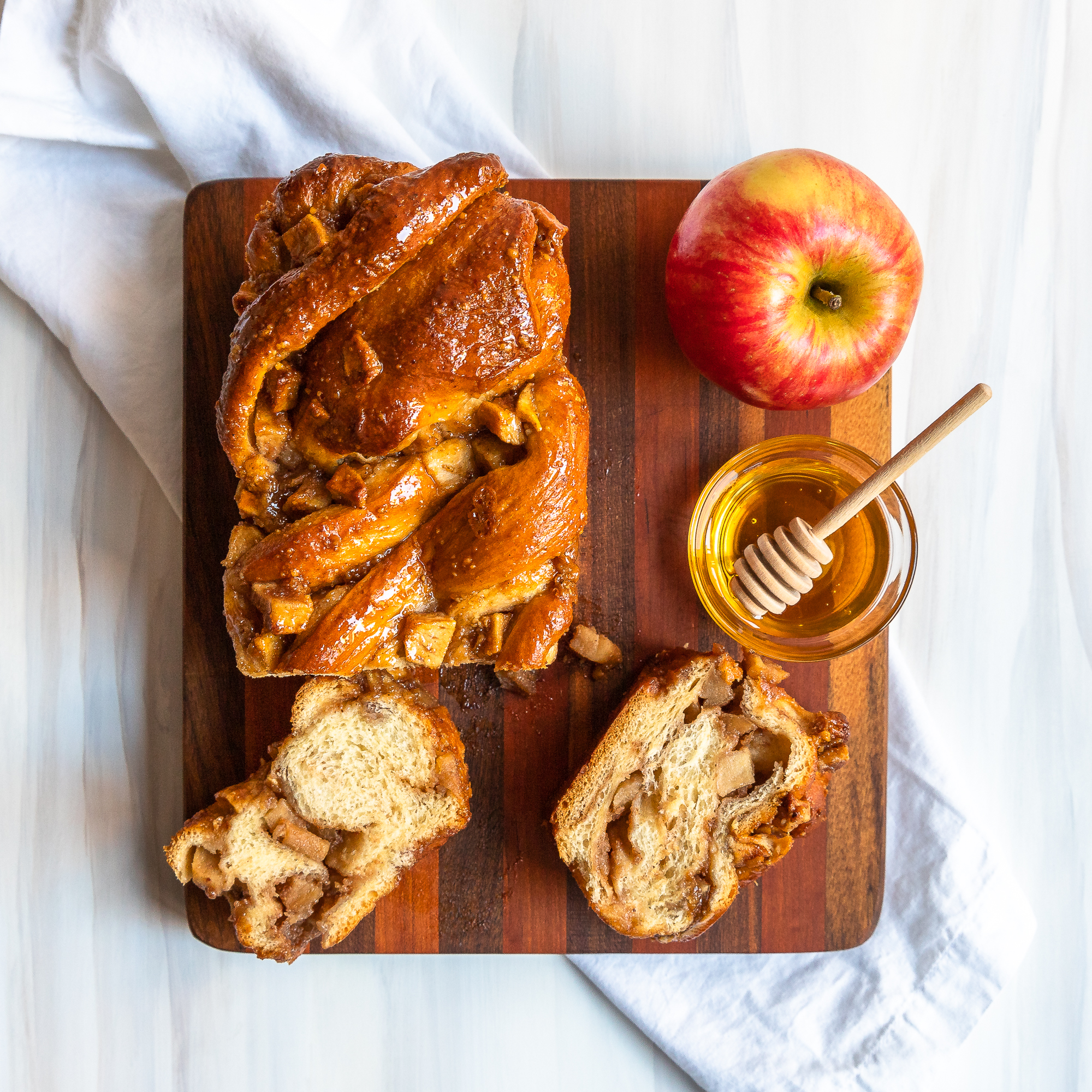 overhead view of apple honey babka on cutting board with a couple slices showing the inside, a bowl of honey and an apple
