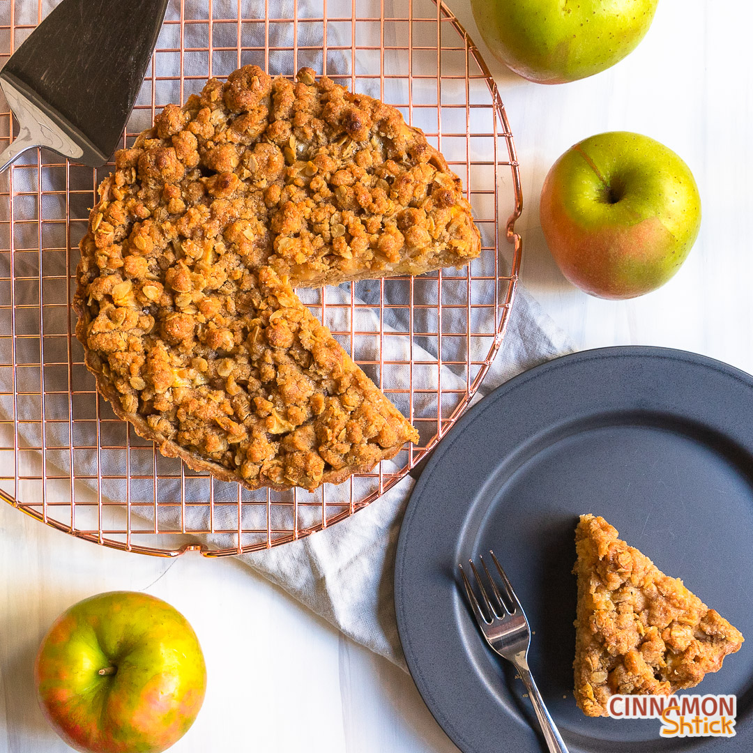 Slice of apple crumb tart on plate next to rest of tart on cooling rack