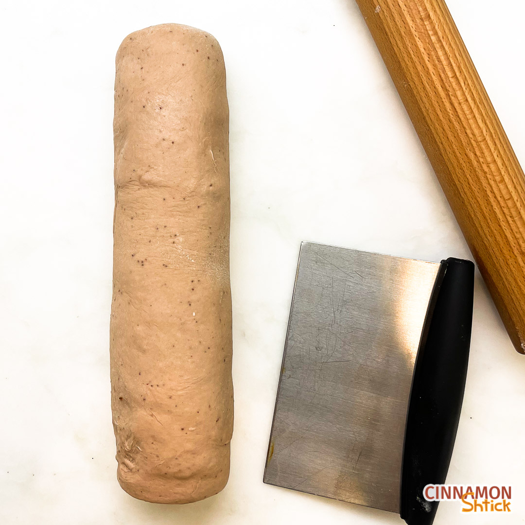 Strawberry fig babka dough rolled into a log with a bench scraper and rolling pin on the side