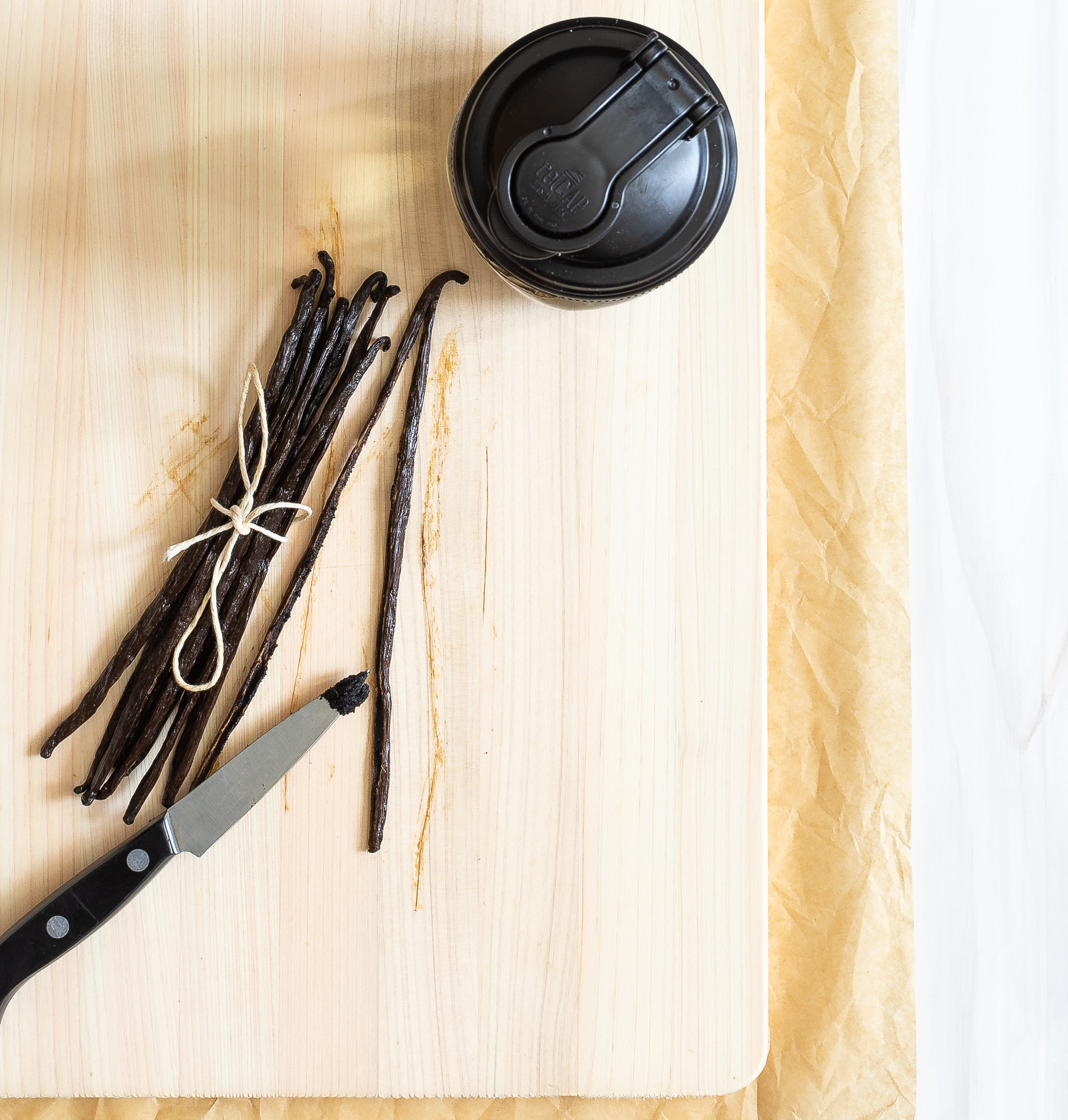 overhead shot showing reCAP lid on a mason jar with a bunch of vanilla beans and a paring knife with vanilla seeds on the tip