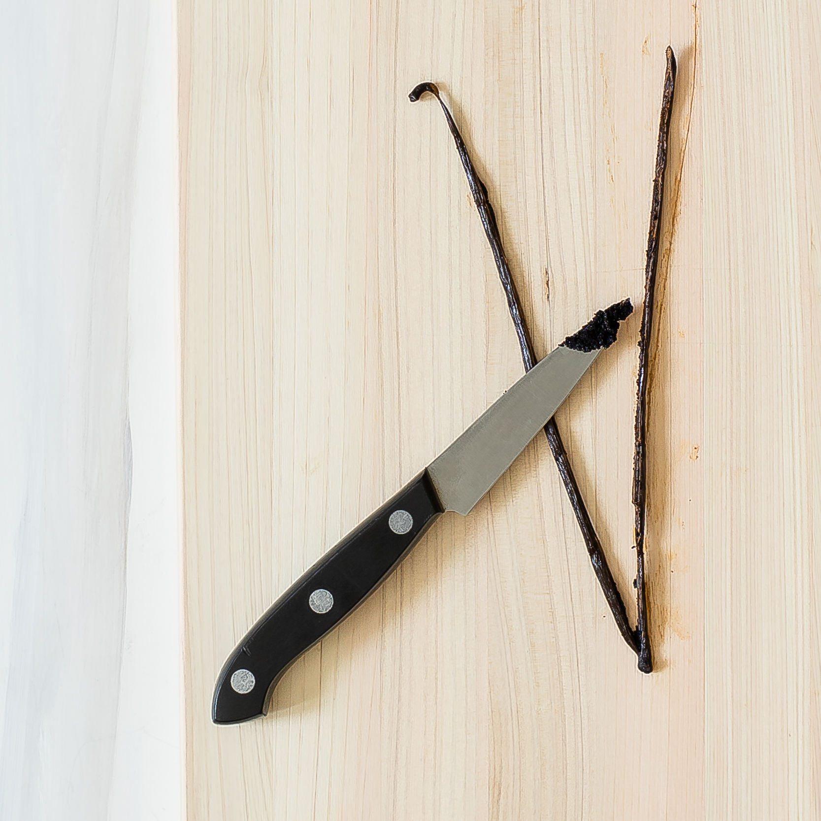 a vanilla bean sliced open with a paring knife showing the seeds on the tip of the knife