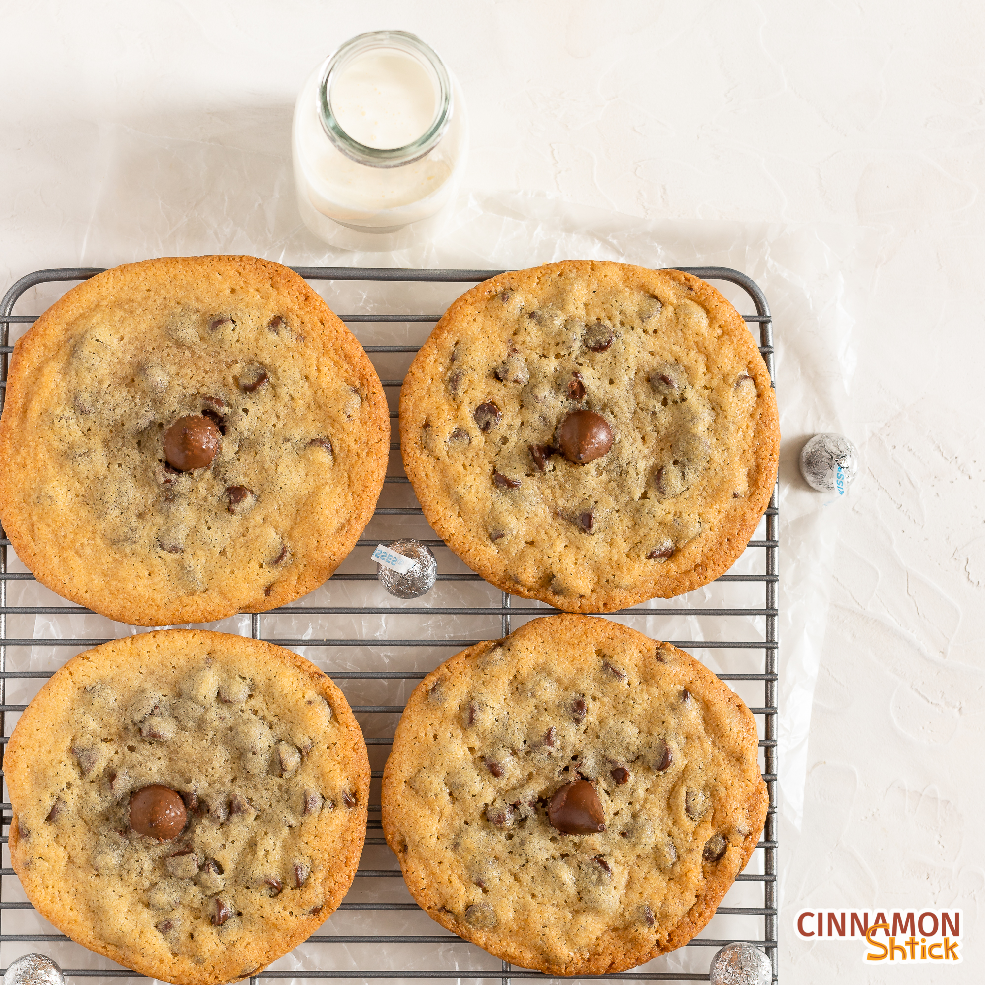 four Big Chipper chocolate chip cookies on a cooling rack with a bottle of milk in top of frame