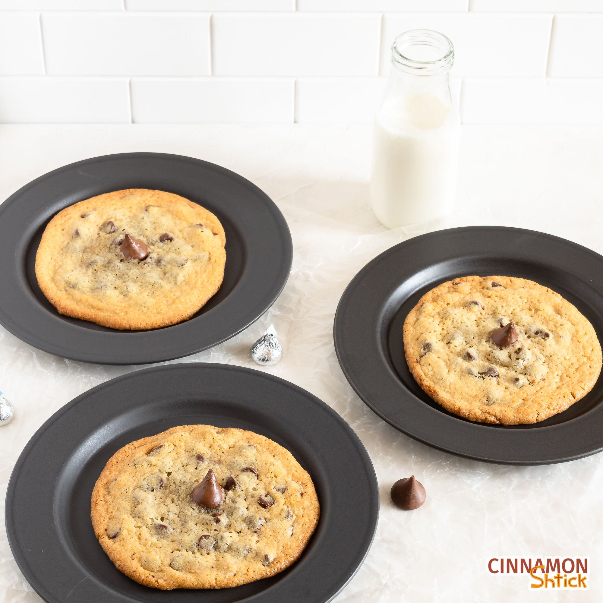 three plated big chipper cookies with a bottle of milk in the background