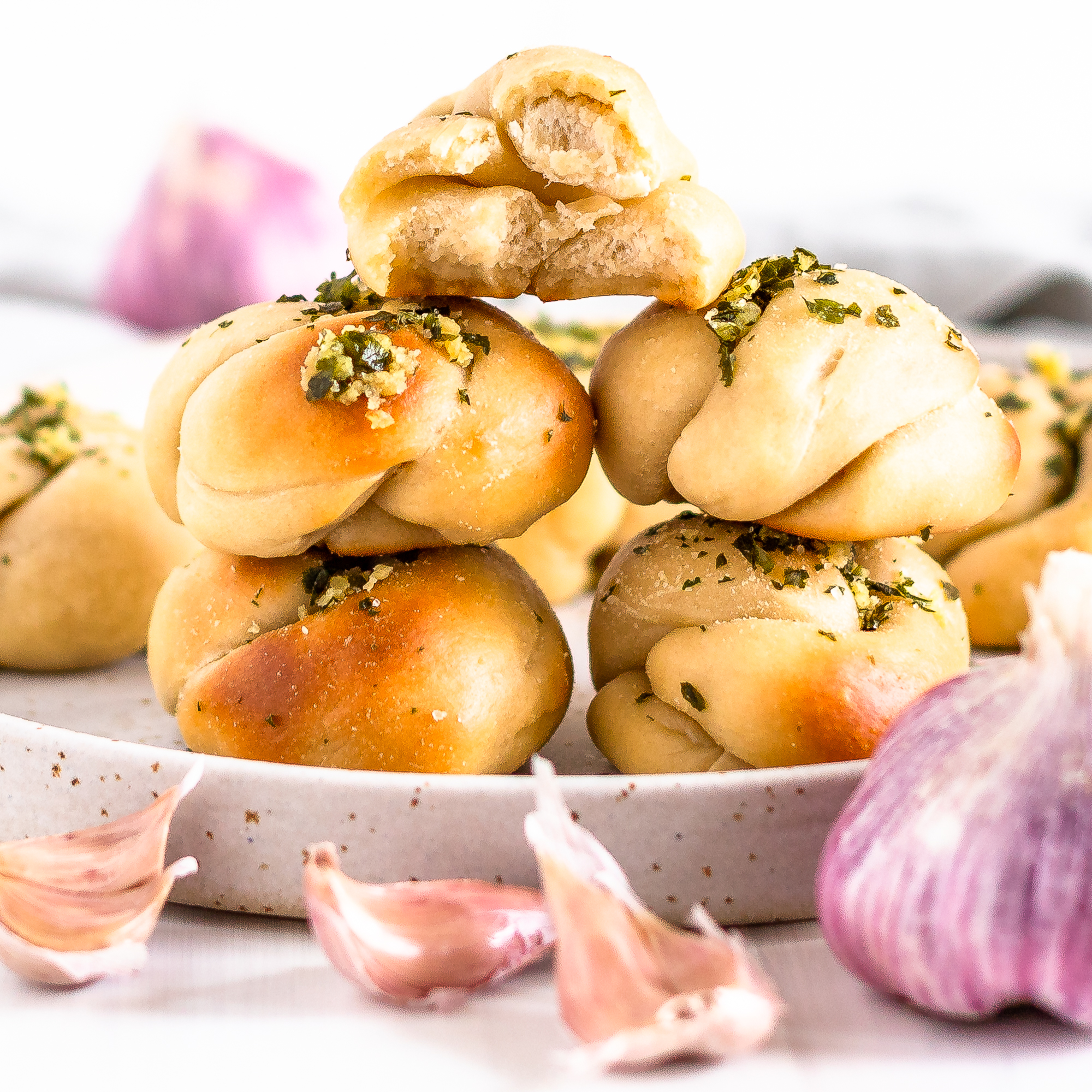 4 sourdough garlic knots stacked in two each next to each other with a garlic knot with a bite taken out on top