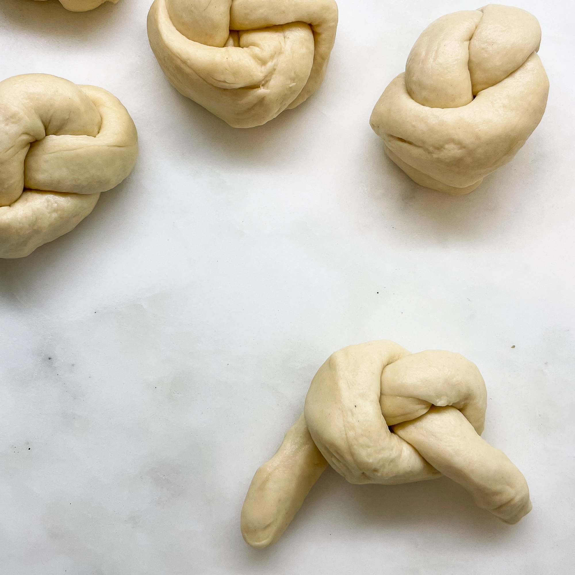 three sourdough discard garlic knots in background with a rope of dough shaped into a knot with the ends hanging to the sides
