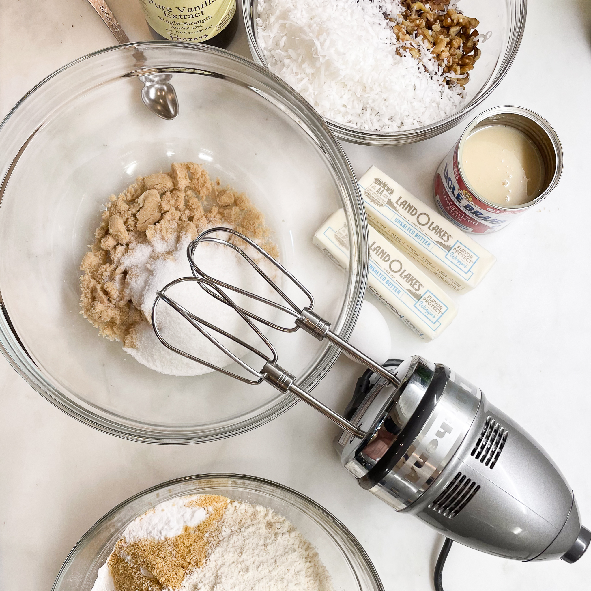 mixer with bowl of sugars, bowl of dry ingredients, bowl of mix-ins, vanilla, butter, condensed milk