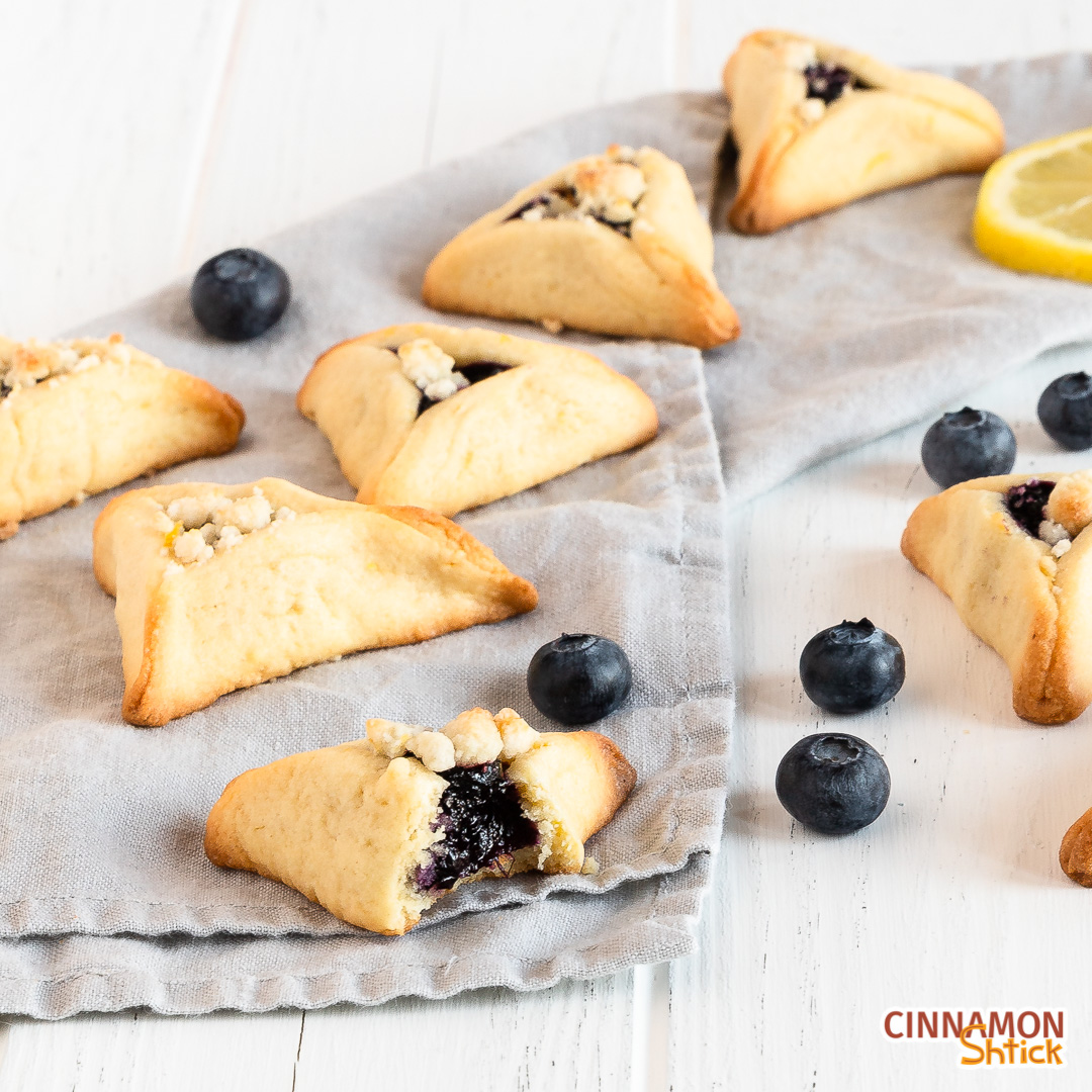 view of diagonal row of blueberry hamantaschen with a bite taken out of the front one showing the blueberry filling