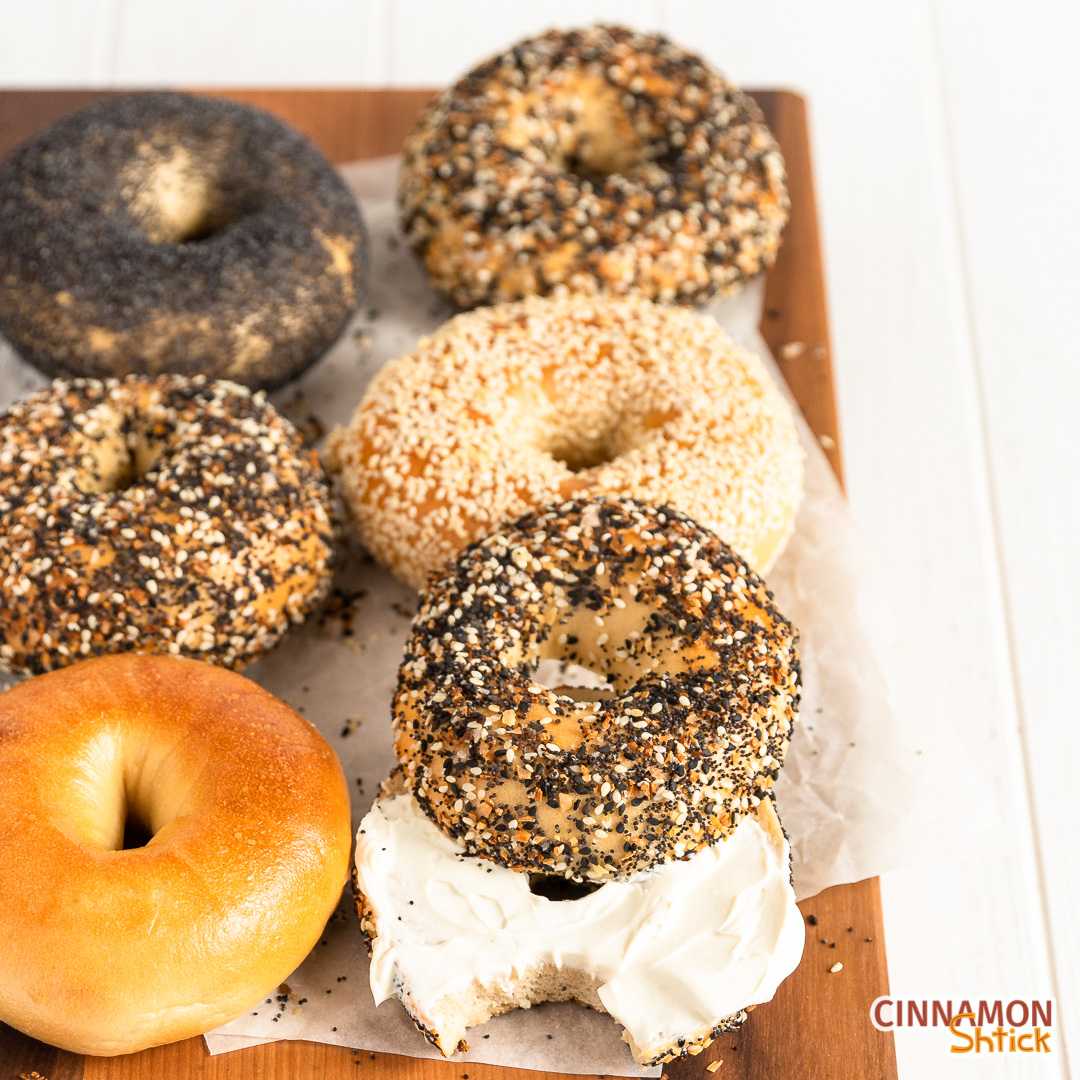 six bagels on cutting board, one of which I cut in half with the top covering half the bottom and the rest of the bottom covered in cream cheese