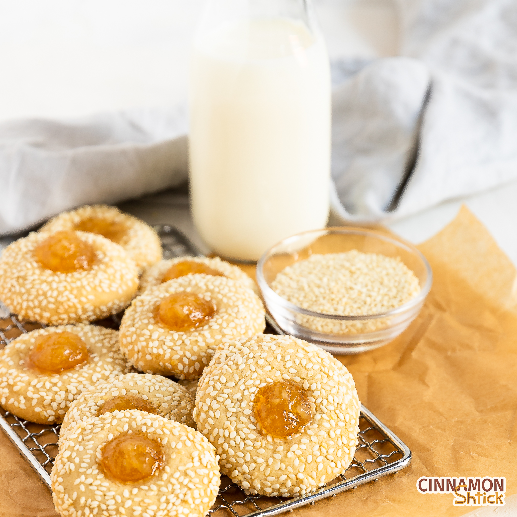 tahini thumbprint cookies on a cooling rack on top of brown parchment paper with a bottle of milk in the right background