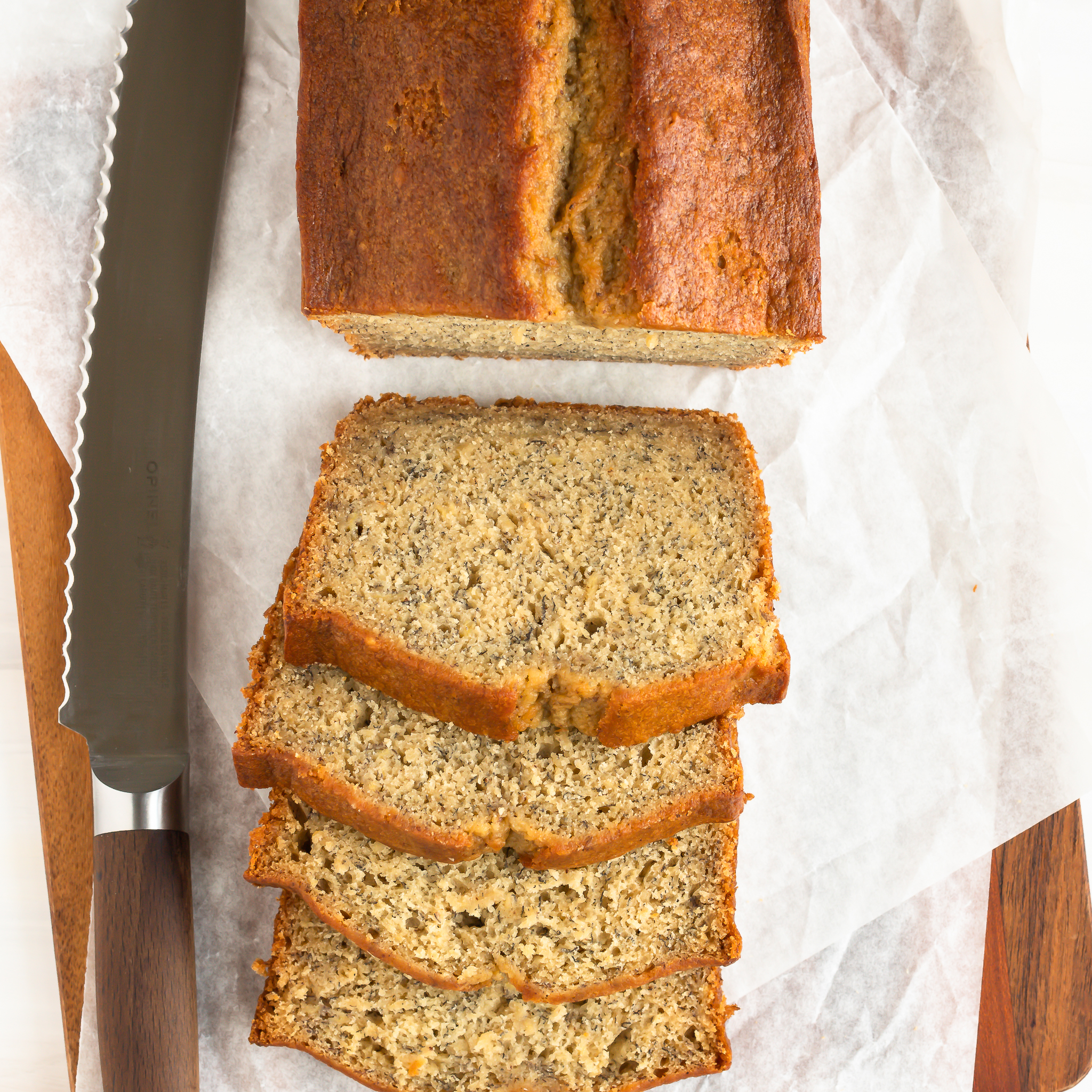 overhead view of slices of banana bread piled against each other and the rest of the loaf with a bread knife to the left