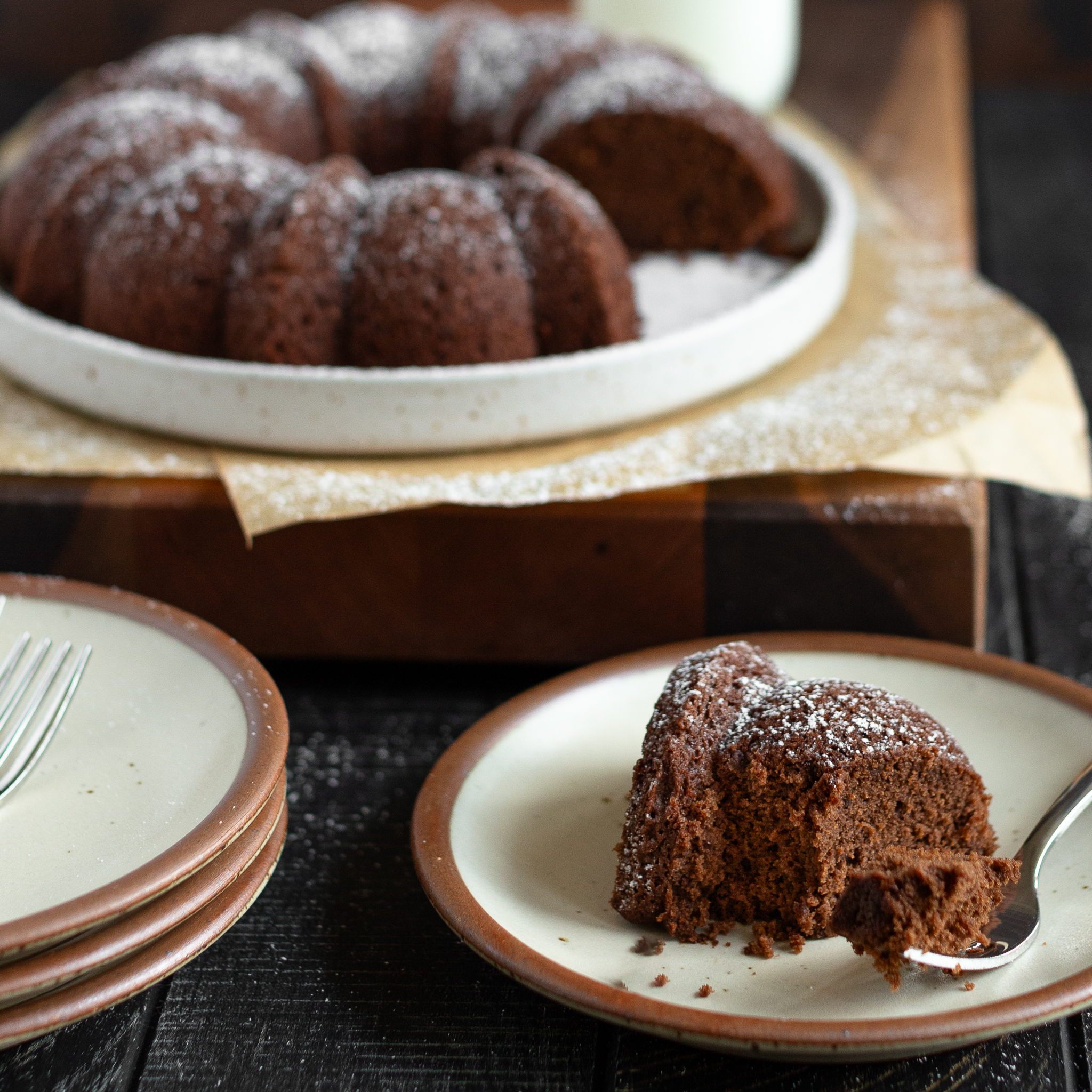 a slice of chocolate egg white cake on a dessert plate with a bite size portion on a fork on the plate. The rest of the cake is in the background.