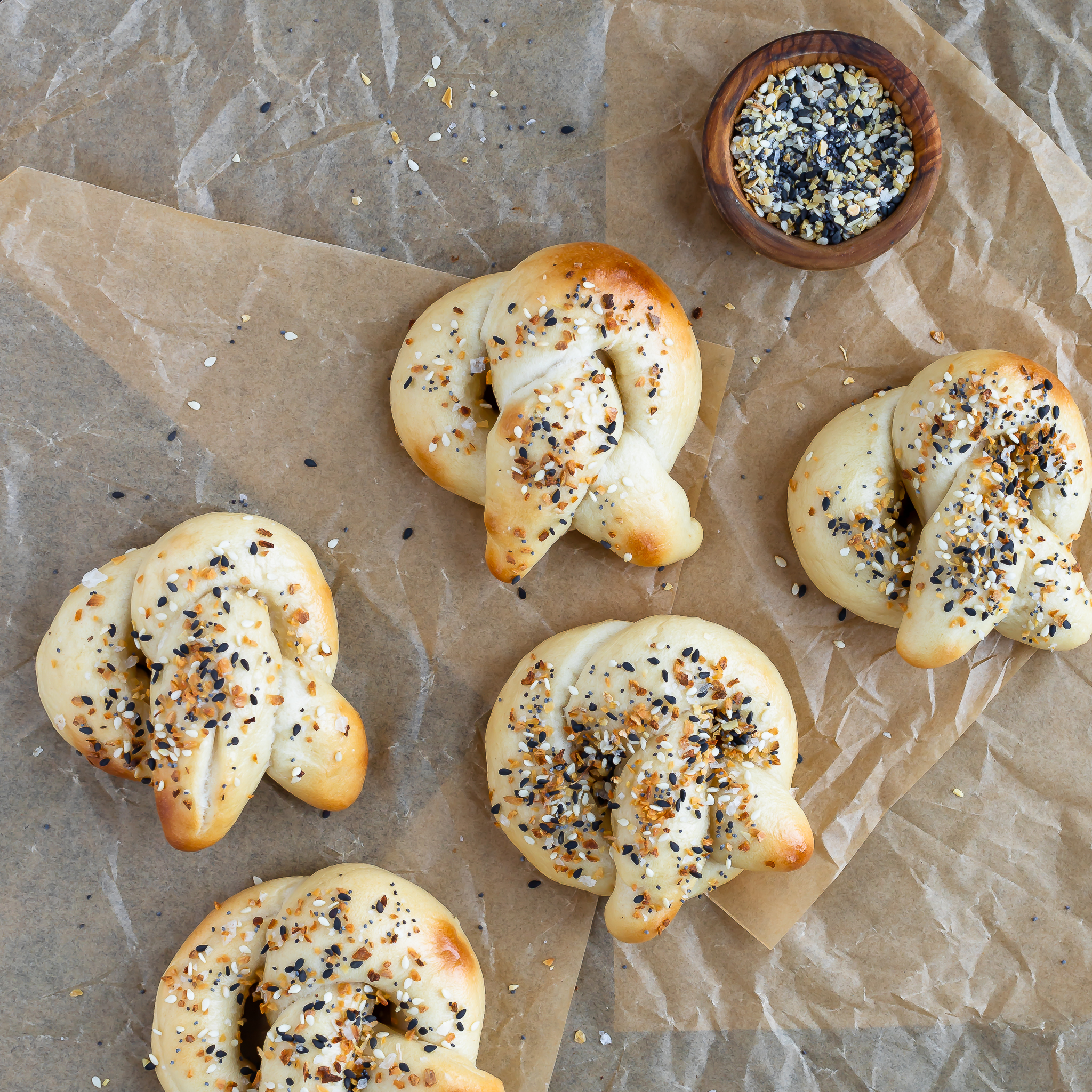 overhead view of sourdough discard pretzels, 3 in a diagonal with 2 above them and a small bowl of everything seasoning