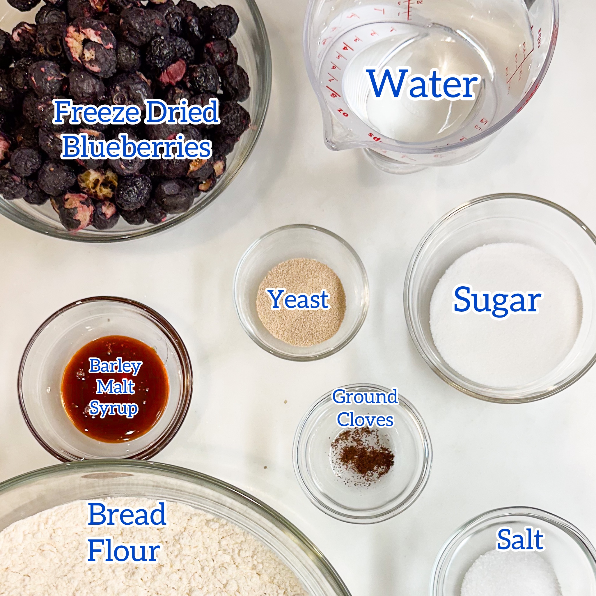 overhead view of bowls containing portioned out ingredients for blueberry bagels: freeze dried blueberries, water, sugar, yeast, ground cloves, salt, bread flour and barley malt syrup.