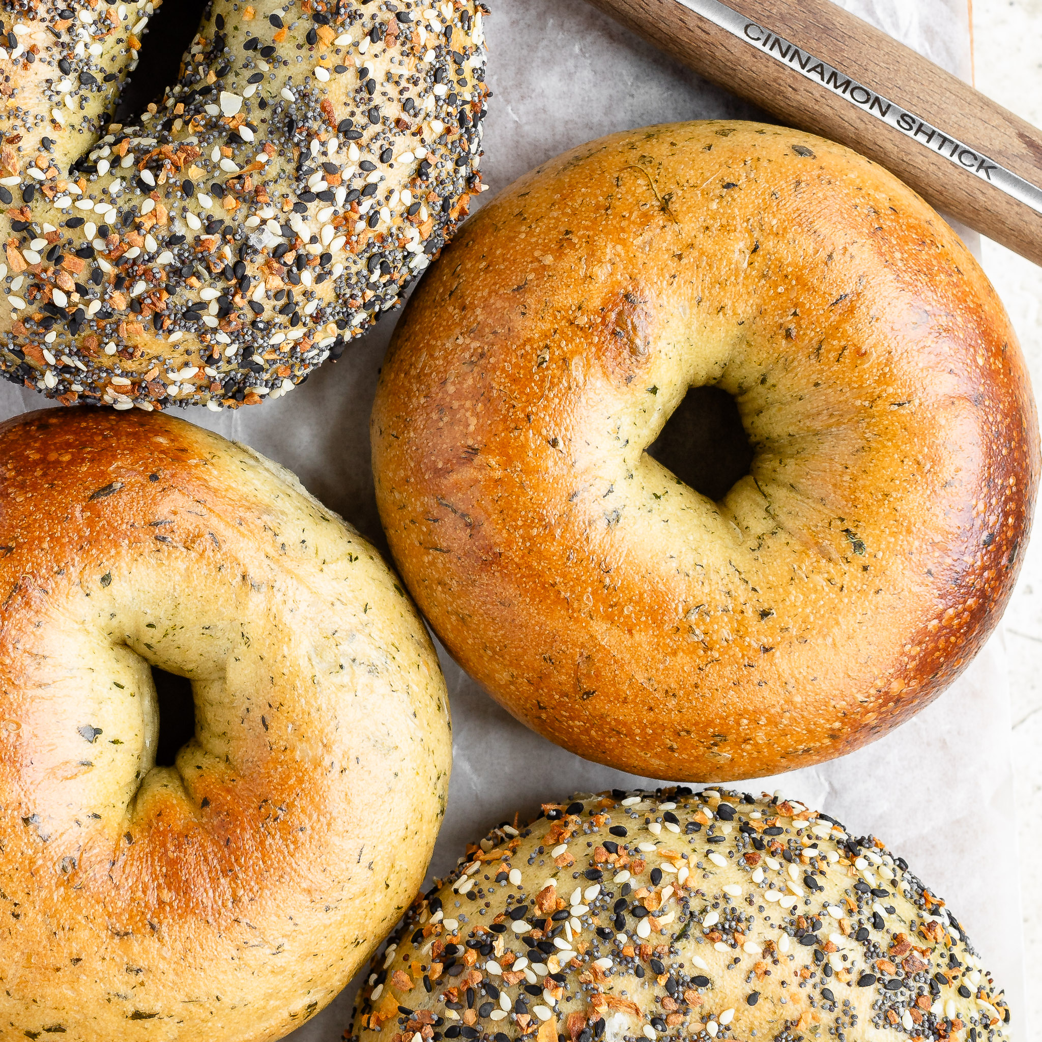 Overhead of 4 spinach bagels, 2 of which are plain and 2 of which are coated with everything seasoning.