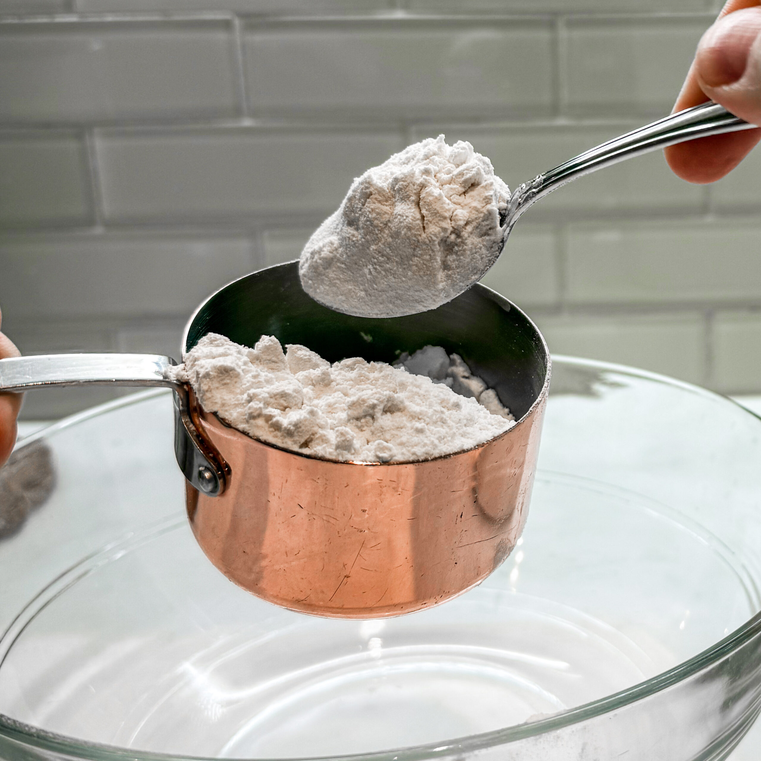A spoonful of flour over a partially filled measuring cup.