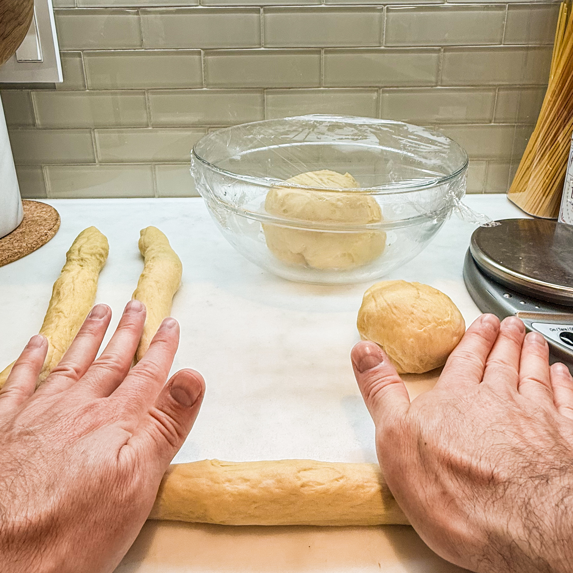 Two hands rolling out the dough with palms of the hands against the countertop.