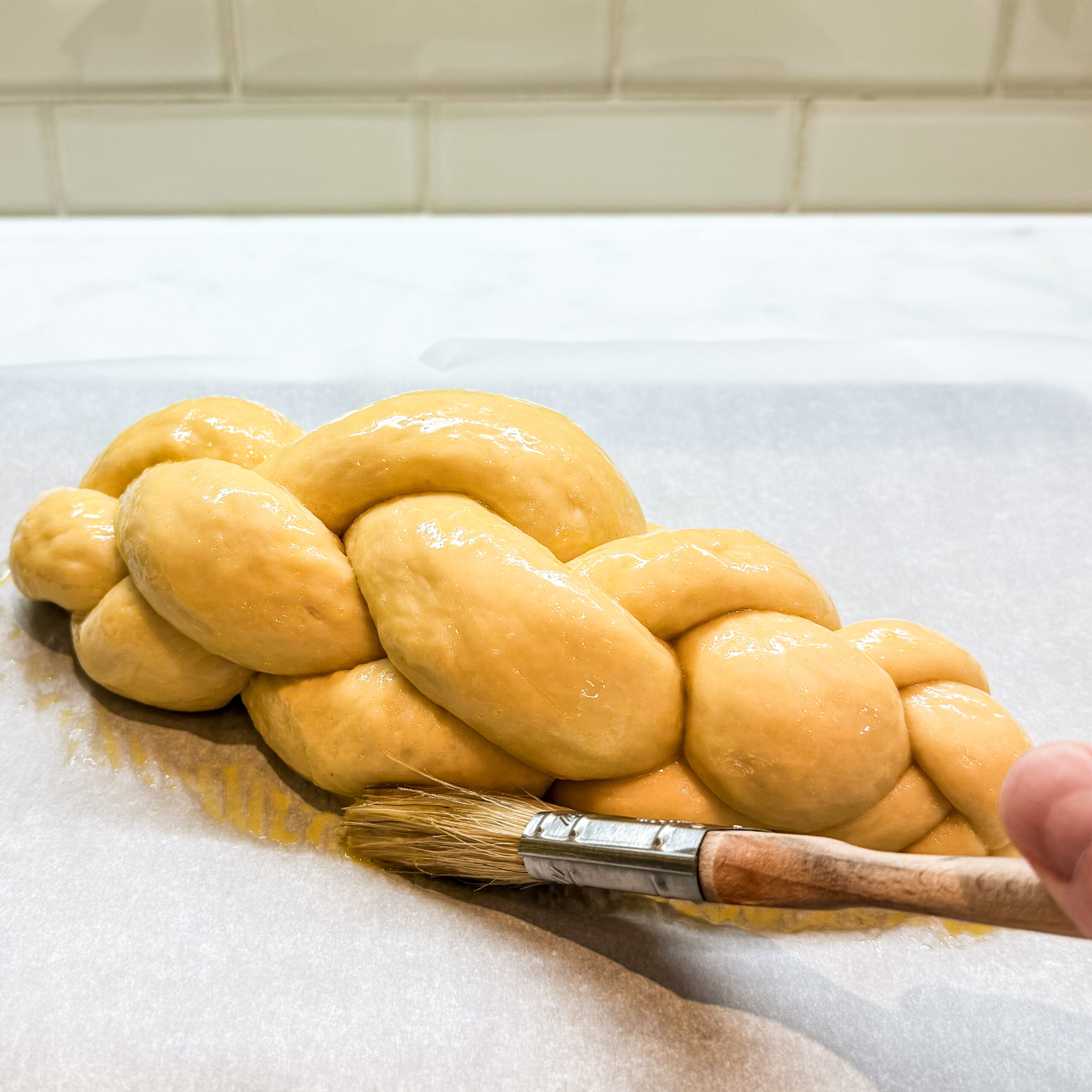 Pastry brush applying egg wash along the bottom edge of the challah dough.