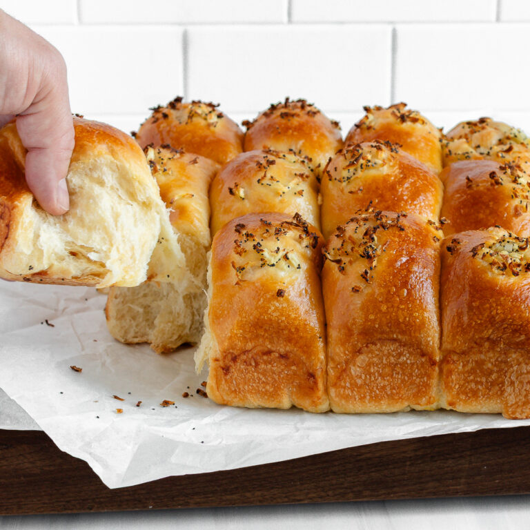 Soft Sourdough Onion Rolls Onion rolls with a hand grabbing a corner roll showing the softness and stretchiness of the inside of the roll.