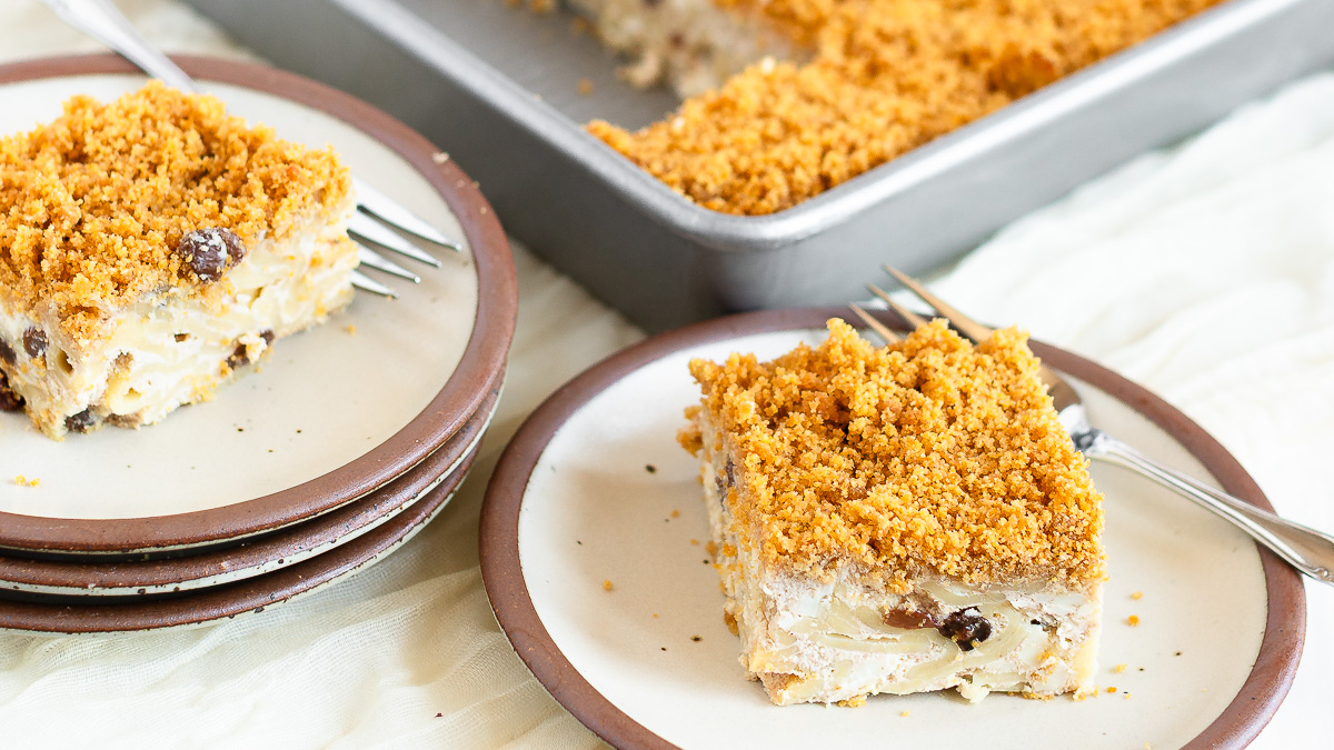 A slice of kugel on a plate with another plated slice and the rest of the pan in the background.